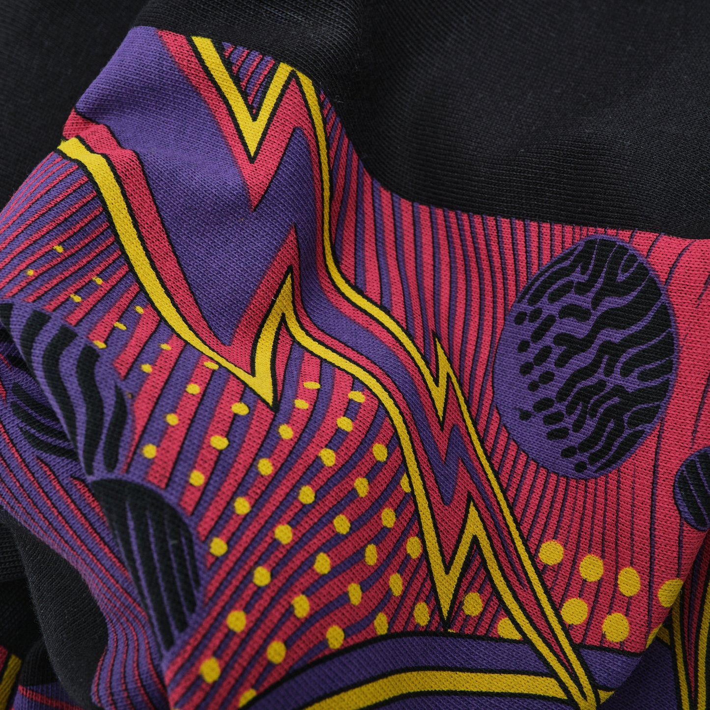 Close-up of a colorful fabric with abstract patterns in red, purple, yellow, and black.